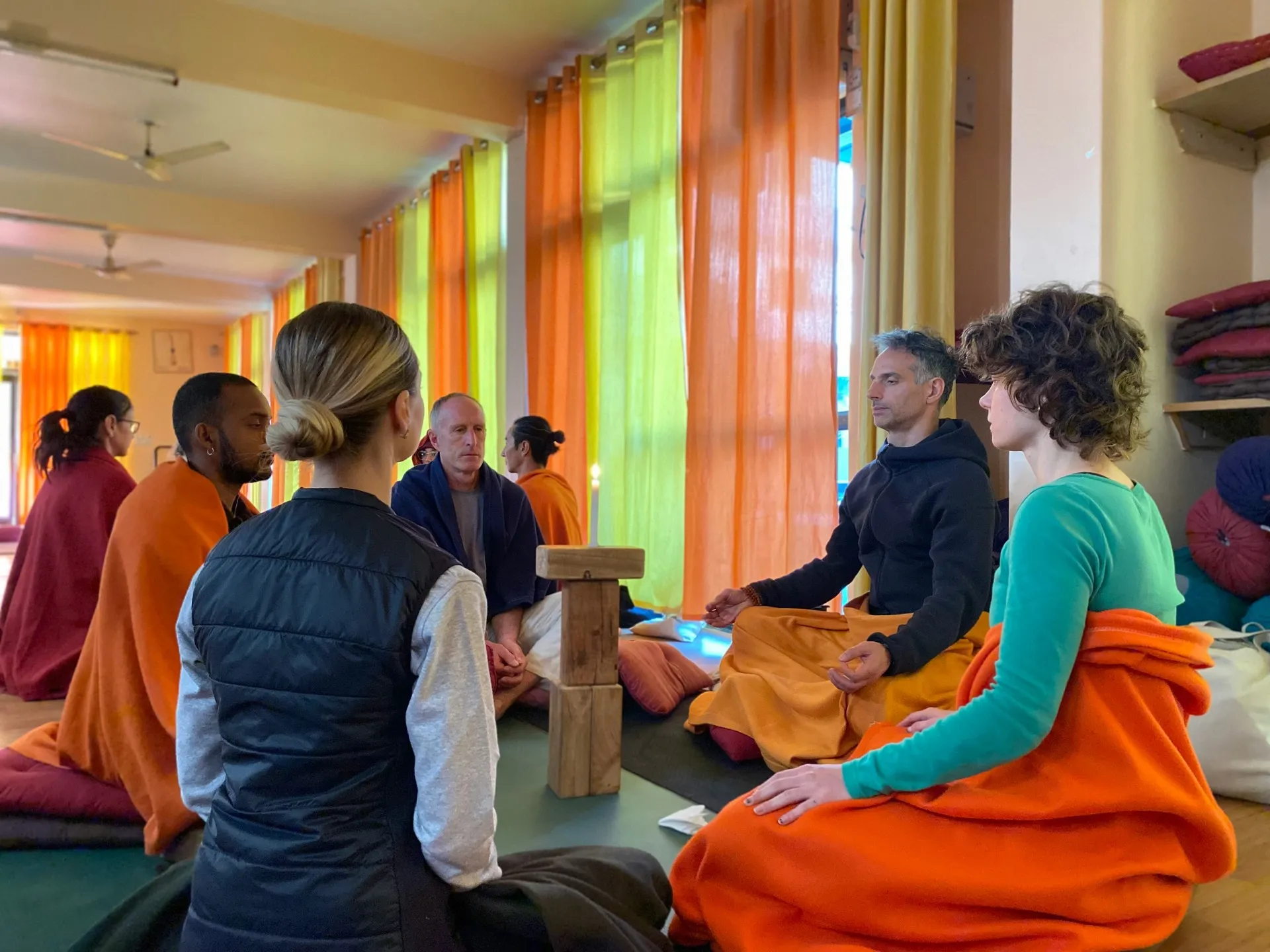 Groep mediteerders in sfeervolle ruimte met kleurrijke stoffen en kussens